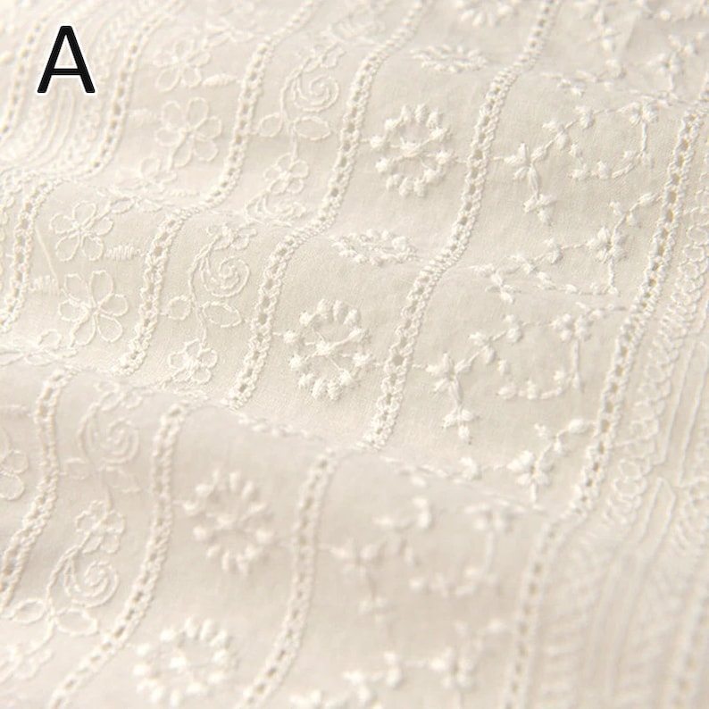 Puede incluir: Tela de algod&oacute;n blanca con un delicado patr&oacute;n bordado de peque&ntilde;as flores y espirales. La tela tiene un brillo sutil y una textura suave.