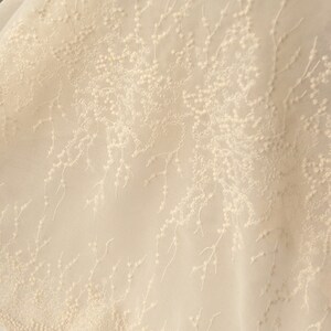 Peut inclure: Gros plan sur un tissu d&eacute;licat de couleur cr&egrave;me avec un motif floral subtil. Le tissu est transparent, presque translucide, et le motif floral est cr&eacute;&eacute; avec de petits points en relief.