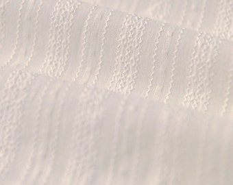 May include: A white fabric featuring a repeating vertical pattern of textured stripes. The design consists of alternating rows of delicate, wavy, zigzag lines and small, raised dot-like stitches, creating a subtle, tactile, and dimensional surface.