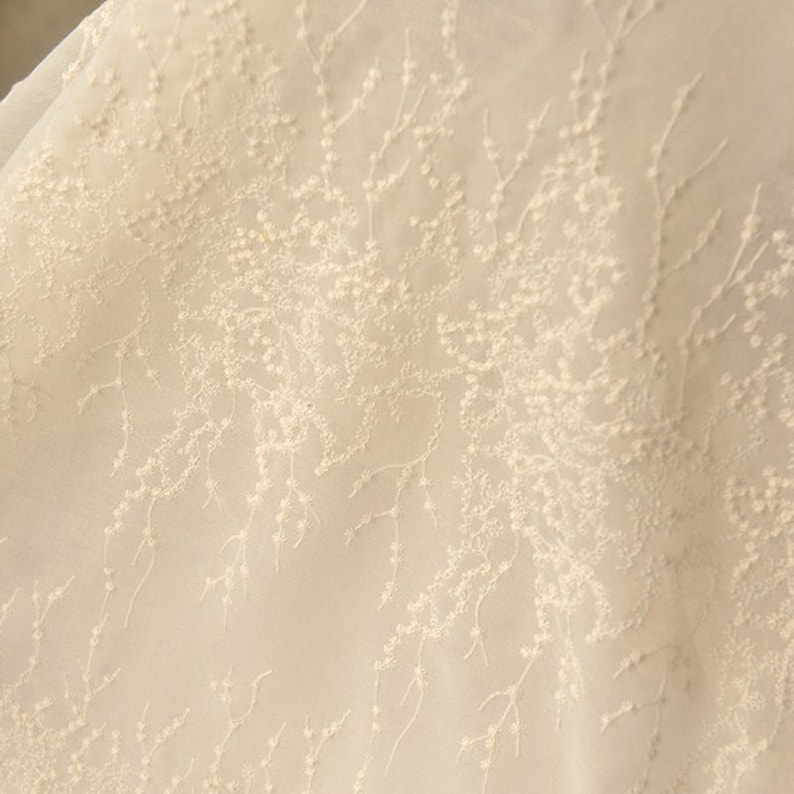 Peut inclure: Tissu blanc transparent avec un motif d&eacute;licat brod&eacute; de petites fleurs blanches et de branches.