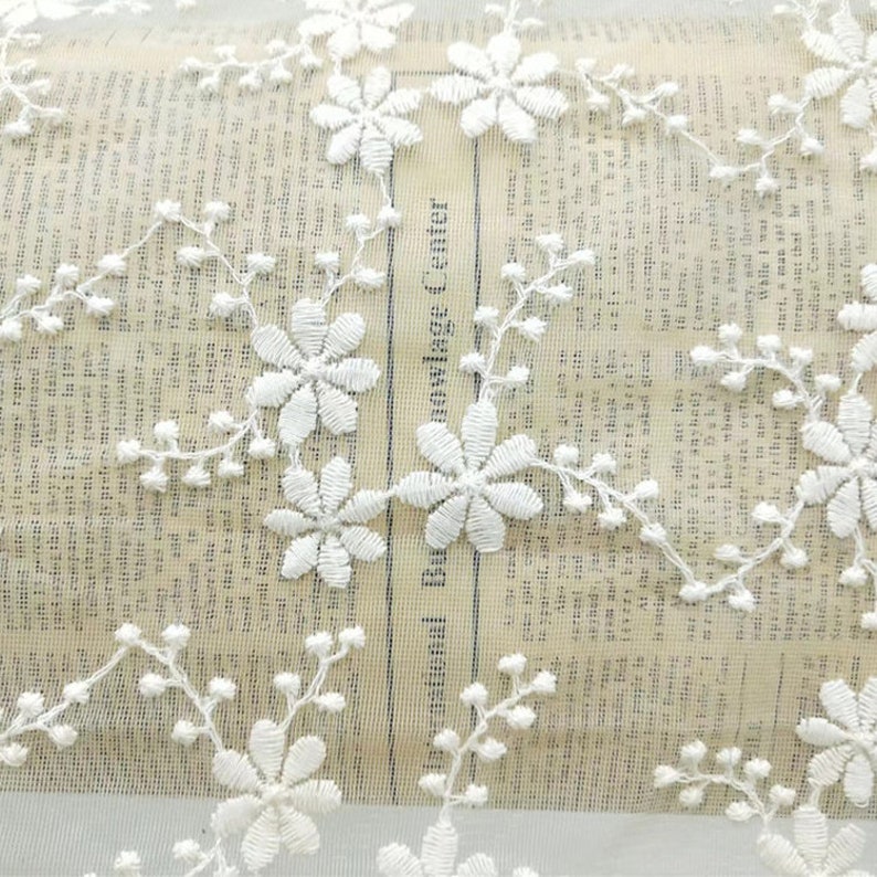 May include: White lace fabric with a delicate floral pattern. The fabric is sheer and has a soft, romantic feel.