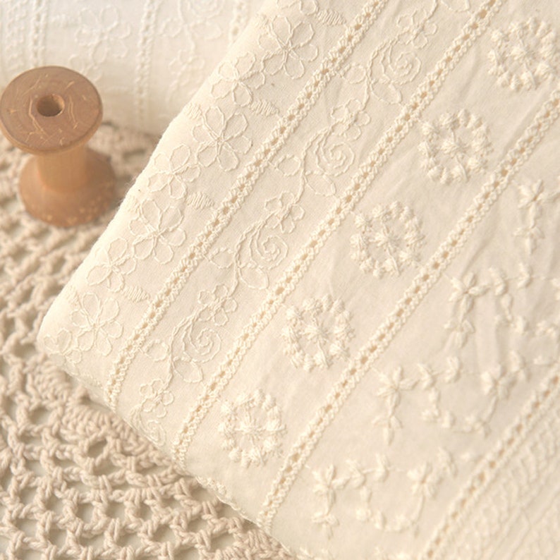 Puede incluir: Tela de algod&oacute;n blanca con delicados patrones florales bordados en un dise&ntilde;o repetitivo. La tela tiene un tacto suave y texturizado, ideal para proyectos de manualidades.