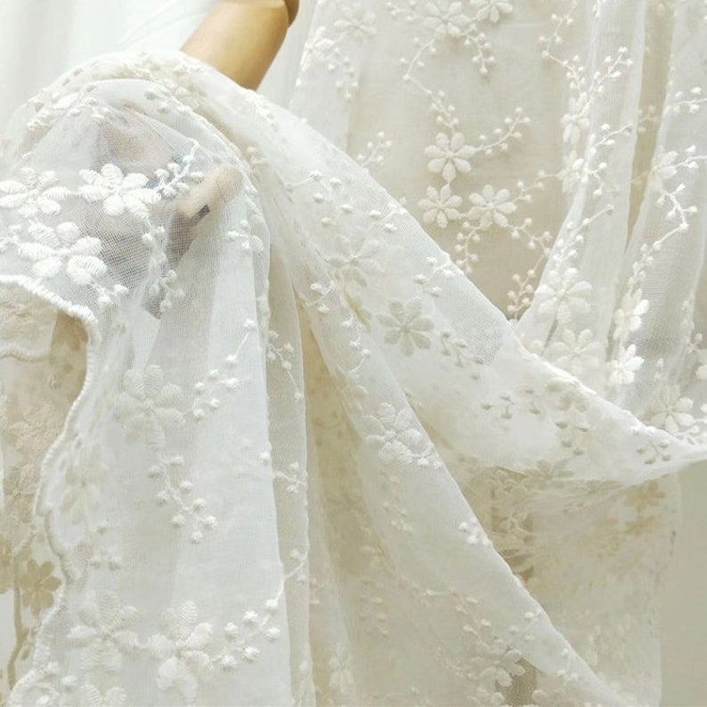 May include: White sheer fabric with delicate floral embroidery. The fabric is soft and lightweight, perfect for creating garments or home decor.