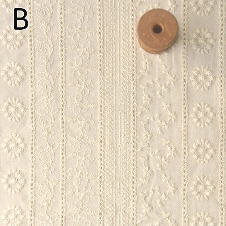 Puede incluir: Tela de algod&oacute;n blanca con patrones florales bordados en rayas verticales. La tela tiene un aspecto delicado y de encaje.