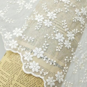 May include: White floral lace trim with a delicate pattern of small flowers and leaves. The lace is on a white background and has a scalloped edge.