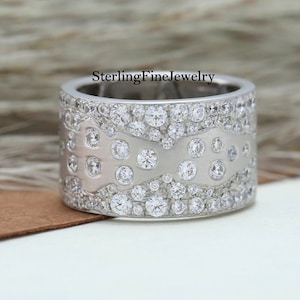 The Diamonds Are Heavily Patterned On The Edges Of The Ring And Then  Around The Center, Round Cut Moissanite Flush And Prong Set Wide Band