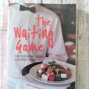 May include: Book cover for "The Waiting Game: The Essential Guide for Wait Staff." The cover shows a server in a white shirt and black bow tie holding a tray with a plate of salad. Authors are Mike Kirkham, Peggy Weiss, & Bill Crawford.