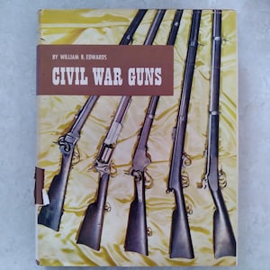 Könnte beinhalten: Ein gebundenes Buch mit dem Titel Civil War Guns von William B. Edwards. Das Cover zeigt einen gelben Hintergrund mit einem braunen horizontalen Band, das den Titel und den Autor enthält. Fünf antike Gewehre sind vertikal abgebildet.