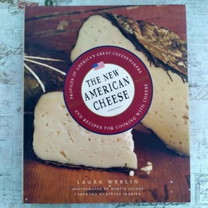 以下が含まれることがあります： 「The New American Cheese」というタイトルと、アメリカ国旗の円形エンブレムが特徴の書籍の表紙。木製の表面にチーズの画像が表示されています。著者はローラ・ワーリンです。