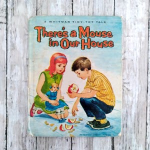 May include: Vintage children's book titled "There's a Mouse in Our House." The cover features illustrations of a girl with red hair holding a doll, and a boy examining an apple. The book has a light blue background with the title in orange and red.