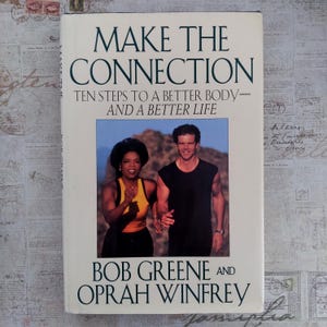 May include: A book cover with the title "MAKE THE CONNECTION" in large, dark green letters. Below, the text reads "TEN STEPS TO A BETTER BODY - AND A BETTER LIFE." The cover features a photo of Oprah Winfrey and Bob Greene.