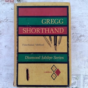 May include: Vintage "Gregg Shorthand" book with a yellow, red, and green cover. The cover features the title, "Gregg Shorthand," and the text "Functional Method" and "Diamond Jubilee Series." The book also displays illustrations of pens and the Gregg logo.