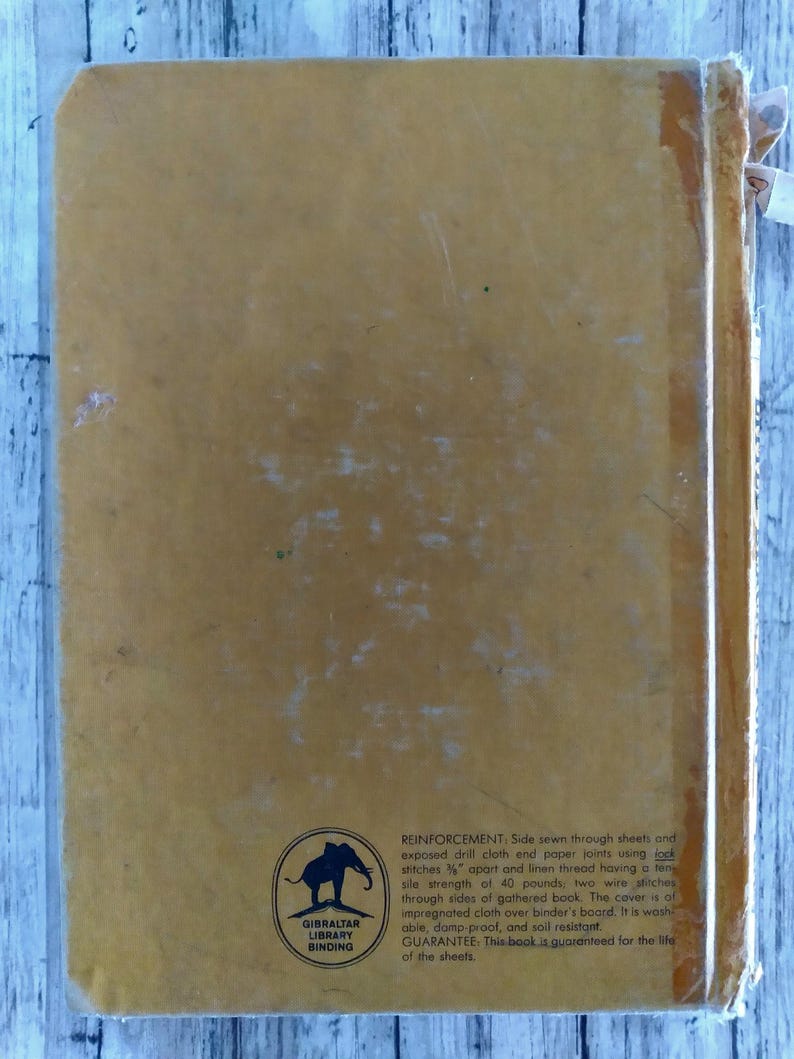 Pu&ograve; includere: Una copertina di libro vintage color giallo senape. Presenta testo e un logo con un elefante. Il testo descrive la rilegatura e la durata del libro, inclusa la sua resistenza al lavaggio e allo sporco. Il libro &egrave; garantito a vita.