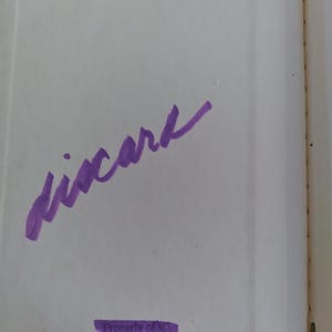 Pu&ograve; includere: Pagina di libro aperta con testo manoscritto viola che recita "xicark". Sotto il testo c'&egrave; un rettangolo viola con la scritta "Property of" e "Public Grade School".