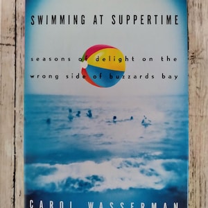 Puede incluir: Portada de libro con una escena de playa azul y blanca, una colorida pelota de playa y el título "SWIMMING AT SUPPERTIME". También se muestra el nombre de la autora, Carol Wasserman, y su afiliación a NPR. El tema del libro parece estar relacionado con el verano o las actividades de playa.