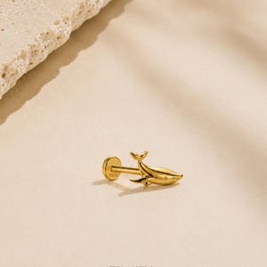 May include: A gold-toned stud earring featuring a small whale charm. The flat circular back of the earring is clearly stamped with the text S925, indicating sterling silver construction. The piece has a polished finish and a simple post design.