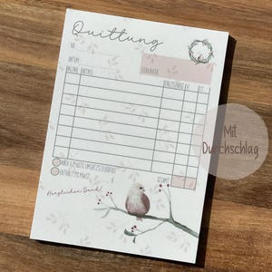 Könnte beinhalten: Ein weißes Quittungsbuch mit floralem Design und einer Vogel-Illustration. Das Buch hat einen Bereich für Datum, Nummer, Anzahl, Artikel, Verkäufer, Einzelpreis und Gesamt. Der Text "Quittung" befindet sich oben auf der Seite. Der Text "Mit Durchschlag" befindet sich unten auf der Seite.