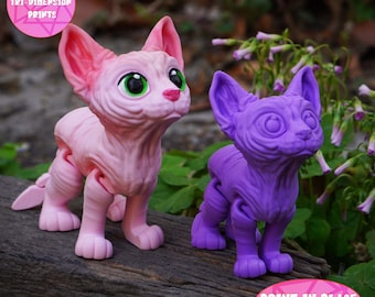 Puede incluir: Dos figuritas de gato articuladas impresas en 3D, una rosa y otra morada, posadas sobre una superficie de madera con vegetación verde en el fondo. El texto "TRI-DIMENSION PRINTS" está en un círculo rosa en la esquina superior izquierda de la imagen. El texto "PRINT.IN.PLACE NO SUPPORTS" está en un triángulo rosa en la esquina inferior derecha de la imagen.