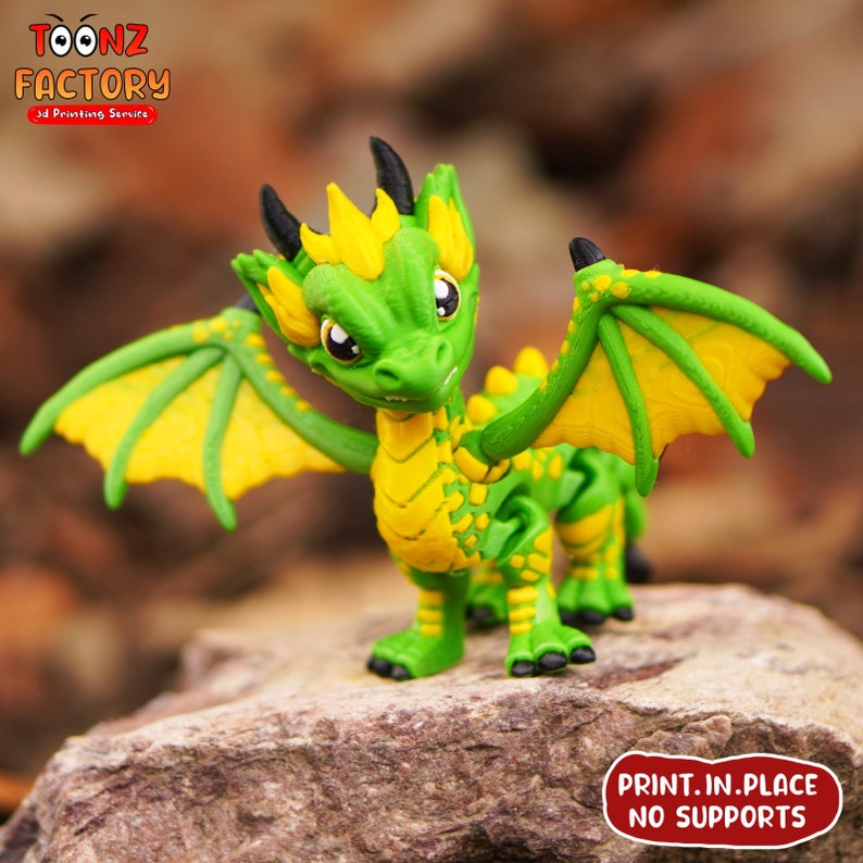 K&ouml;nnte beinhalten: Eine 3D-gedruckte Drachenfigur in Gr&uuml;n und Gelb mit ausgebreiteten Fl&uuml;geln. Der Drache hat einen stacheligen Kamm und ein zahniges Grinsen. Der Text "PRINT. IN. PLACE NO SUPPORTS" ist auf der Basis aufgedruckt.