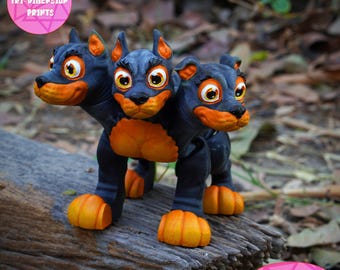 May include: A three-headed dog figurine with black and orange paint. The figurine is printed in place, meaning it does not require supports. The figurine is sitting on a log.