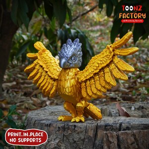 May include: A golden griffin figurine with outstretched wings, a silver head, and detailed feather textures. The figurine is 3D printed and stands on a tree stump. The image includes the text "TOONZ FACTORY 3D Printing Service" and "PRINT.IN.PLACE NO SUPPORTS".