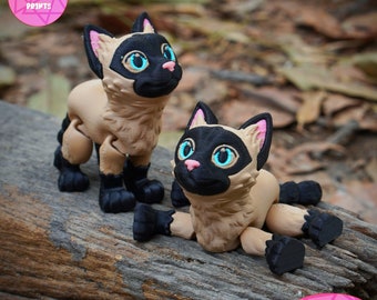 May include: Two 3D printed Siamese cat figurines, one standing and one lying down. Both cats have black ears, noses, and paws, and blue eyes. The figurines are printed in a light brown color. The text "PRINT IN PLACE NO SUPPORTS" is printed on the bottom of the image.