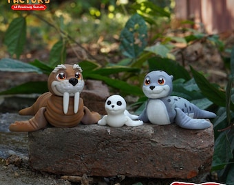 May include: Three 3D printed animal figurines: a brown walrus with large tusks, a gray seal with a white belly, and a smaller white seal. The figurines are posed on a brown brick surface with green foliage in the background. The text "PRINT.IN.PLACE NO SUPPORTS" is printed on the brick surface.
