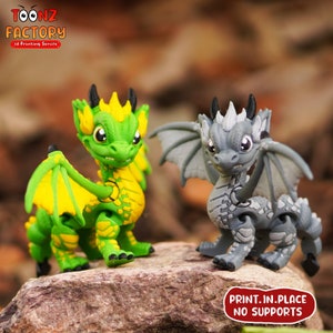 K&ouml;nnte beinhalten: Zwei 3D-gedruckte Drachenfiguren, eine gr&uuml;n mit gelben Akzenten und die andere grau mit wei&szlig;en Akzenten. Beide Drachen haben Fl&uuml;gel und stehen in einer stehenden Position. Der Text "PRINT.IN.PLACE NO SUPPORTS" ist unten im Bild gedruckt.