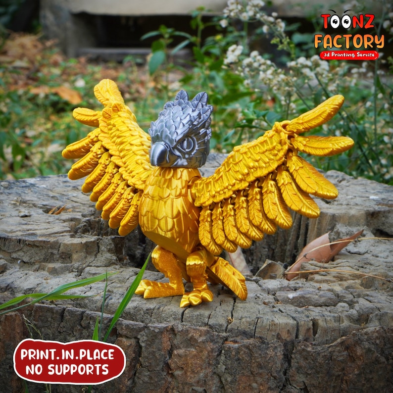 May include: A golden griffin figurine with outstretched wings, a silver head, and detailed feather textures. The figurine is 3D printed and sits on a tree stump. The text "PRINT.IN.PLACE NO SUPPORTS" is visible.