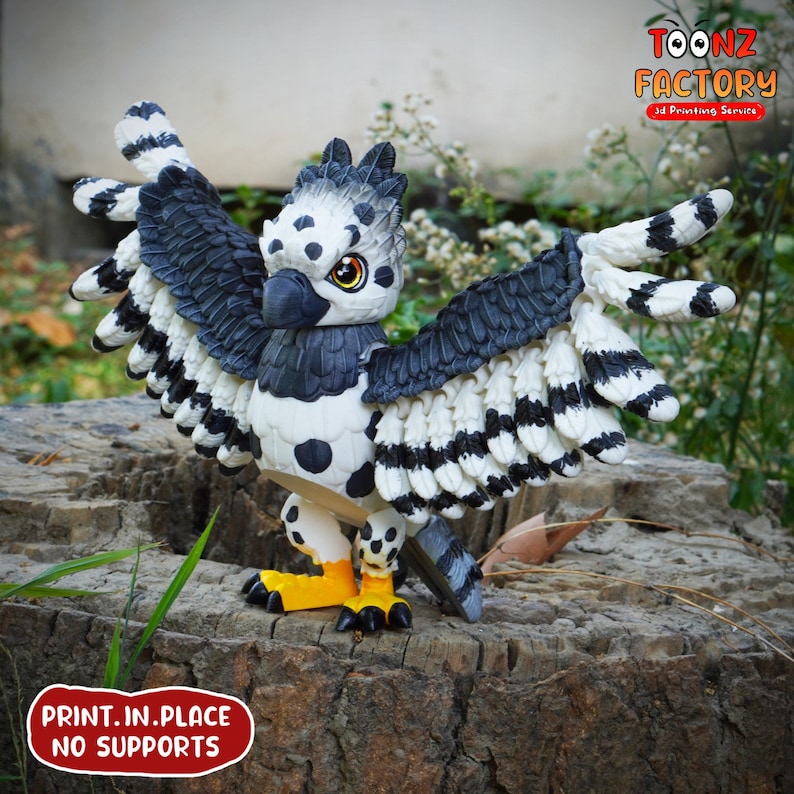 May include: A 3D-printed figurine of a stylized bird with outstretched wings. The bird features a black, white, and gray color scheme with yellow feet and a detailed design. The text "PRINT.IN.PLACE NO SUPPORTS" is visible.