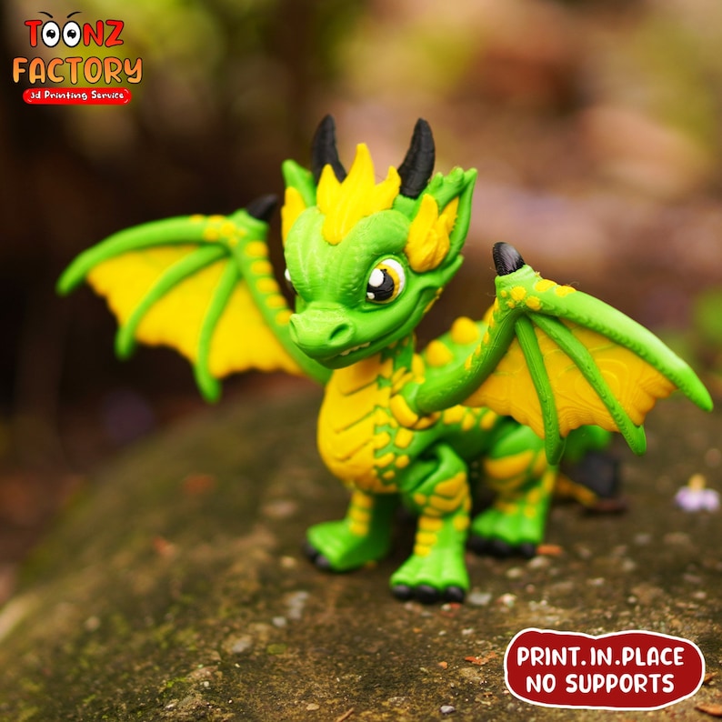 K&ouml;nnte beinhalten: Eine gr&uuml;n-gelbe 3D-gedruckte Drachenfigur mit ausgebreiteten Fl&uuml;geln. Der Drache hat ein zahniges Grinsen und gro&szlig;e Augen. Der Text "PRINT. IN. PLACE NO SUPPORTS" ist auf der Basis aufgedruckt.