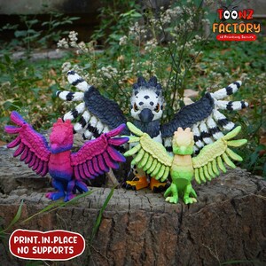 May include: A collection of colorful 3D-printed bird figurines with outstretched wings. The birds are in shades of pink, blue, green, and yellow, with black and white accents. The text "PRINT.IN.PLACE NO SUPPORTS" is visible.