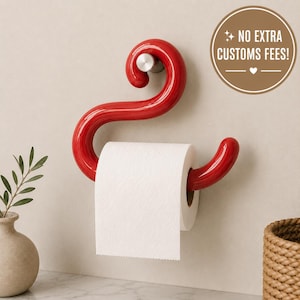 Könnte beinhalten: Ein glänzender, S-förmiger Toilettenpapierhalter zur Wandmontage in Rot mit einem silberfarbenen Befestigungselement. Eine Rolle weißes Toilettenpapier hängt am unteren Arm. Ein kreisförmiges Abzeichen zeigt den Text NO EXTRA CUSTOMS FEES!