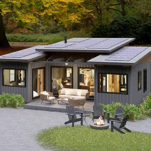 May include: A modern, gray-sided house with a flat roof covered in solar panels. The house has large windows and a patio with outdoor furniture, including chairs, a sofa, and a fire pit. The setting is a grassy area with trees.