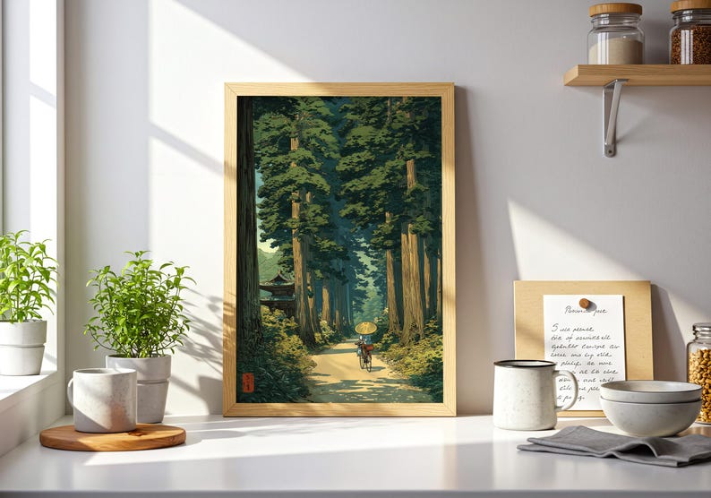 Japanese-inspired art print of an elderly lady cycling through a lush green forest, traditional style poster with calming nature tones, shown framed and displayed in a white kitchen