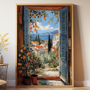 以下が含まれることがあります： 青い窓枠から見える風景を描いた額装アートプリント。オレンジの木、赤い屋根、青い空の下の海の景色がある沿岸の町が描かれています。フレームは明るい木の色です。