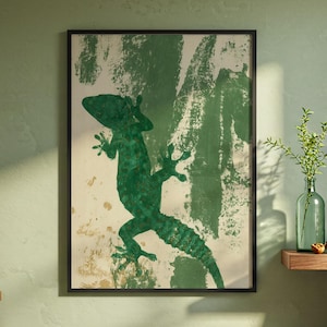 May include: A framed wall art print featuring a dark green silhouette of a gecko against a textured, off-white background with abstract green brushstroke patterns. The artwork is enclosed in a thin black frame, displaying a high-contrast design.