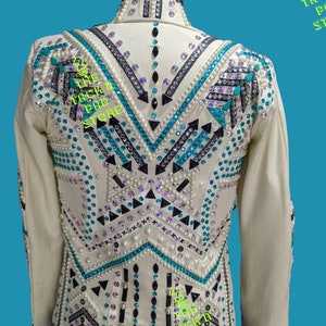 May include: White show jacket with black and turquoise geometric design, embellished with rhinestones and pearls. The jacket has a collar and long sleeves. The text "The Tack Pad Store" is visible on the jacket.