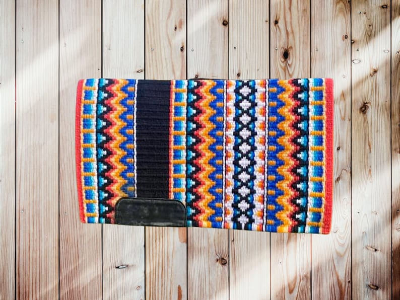 May include: A colourful saddle pad with a geometric pattern in shades of blue, orange, yellow, and white. The pad has a black centre section and a red border.