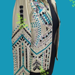 May include: A white leather jacket with turquoise and black geometric designs and pearl embellishments. The jacket has a zipper closure and a collar. The text "THE TACK N PAD STORE" is visible on the jacket.