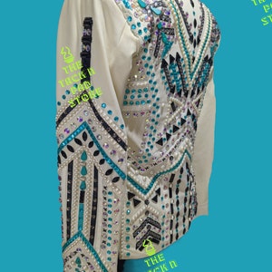 May include: White show shirt with a geometric design featuring black, turquoise, and white rhinestones. The shirt has long sleeves and a collar. The text "THE TACK N PAD STORE" is visible on the shirt.