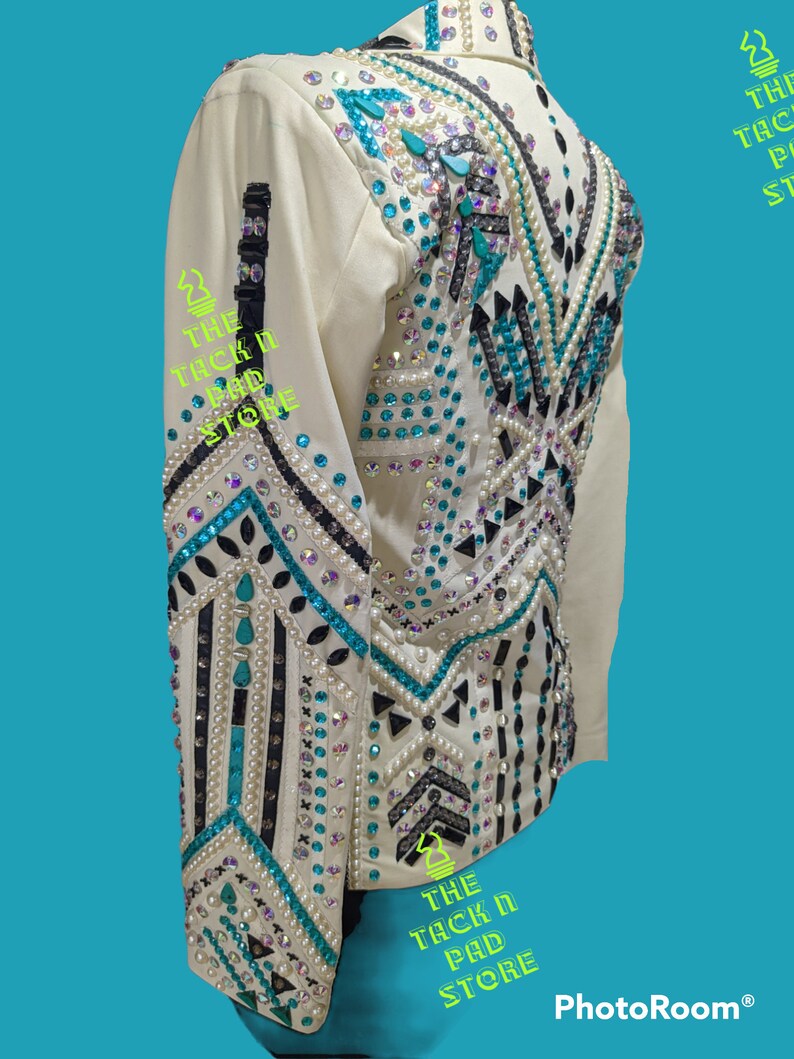 May include: White show shirt with a geometric design featuring black, turquoise, and white rhinestones. The shirt has long sleeves and a collar. The text "THE TACK N PAD STORE" is visible on the shirt.