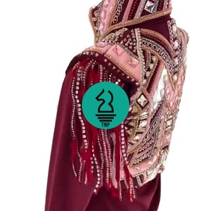 May include: Burgundy show jacket with a pink and gold embellished design. The jacket features a high collar, long sleeves, and fringe detailing on the shoulders.