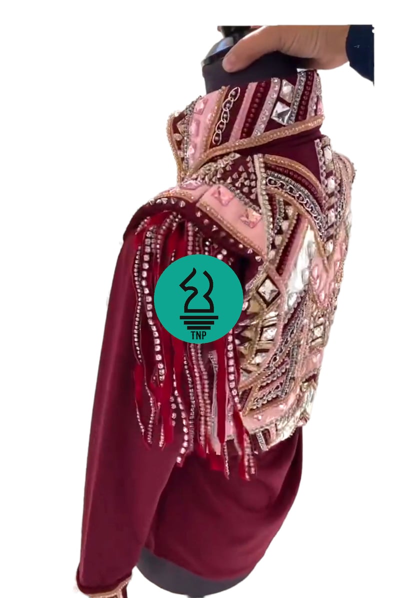 May include: Burgundy show jacket with a pink and gold embellished design. The jacket features a high collar, long sleeves, and fringe detailing on the shoulders.