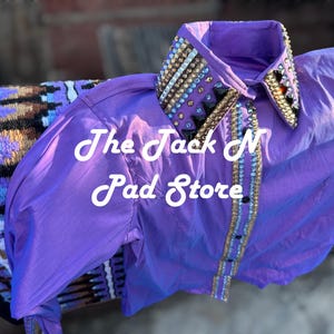 May include: A bright purple shirt with a decorated collar. The collar and front of the shirt are adorned with gold, silver, and black embellishments. The text "The Jack N Pad Store" is visible on the shirt.