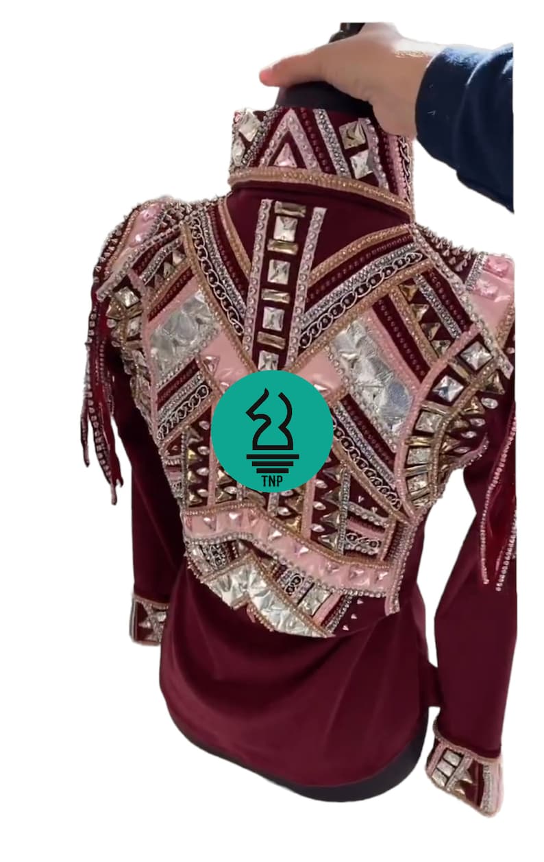 May include: Burgundy show shirt with long sleeves and a pink and gold geometric design with rhinestones and fringe. The shirt has a high collar and a TNP logo on the back.