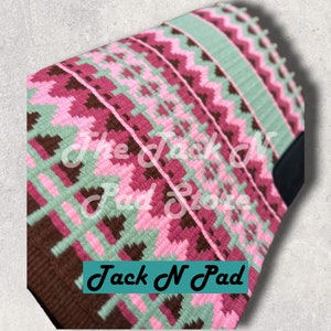 Könnte beinhalten: Ein rosa, grünes und braunes Sattelpad mit geometrischem Muster. Das Pad hat den Text "Jack N Pad" aufgedruckt.