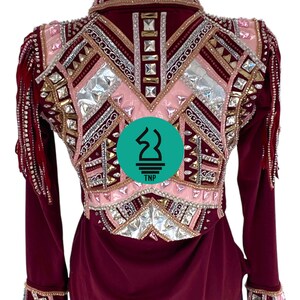 May include: Burgundy long-sleeve shirt with a pink, silver, and gold geometric design featuring rhinestones and fringe. The shirt has a collar and button closure. The back of the shirt features a logo that says "TNP".