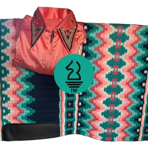 Könnte beinhalten: Ein korallenfarbenes Reitturniershirt mit einem geschmückten Kragen und einem Reißverschluss wird auf einer gemusterten Satteldecke präsentiert. Die Satteldecke hat eine marineblaue Basis mit einem geometrischen Design in Türkis, Koralle und Weiß. Ein schwarzer Lederaufnäher ist sichtbar.