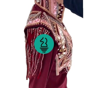 May include: A maroon show shirt with long sleeves and a beaded design. The shirt has a pink and gold trim with rhinestones and fringe. The shirt is on a mannequin.